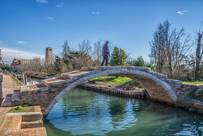 person walking along curved bridge over a river