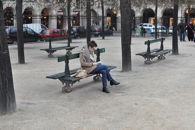 person reading book while sitting on bench in Paris