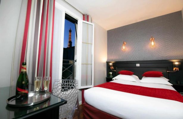 hotel room with white and red bed next to open window with eiffel tower in the distance