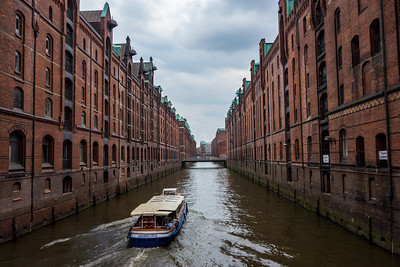 boat sailing on canal between rows of brick warehouse buildings