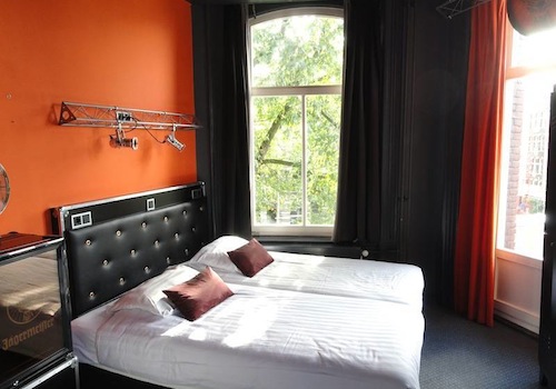 white bed with black leather headboard in room with red walls at BackStage Hotel in Amsterdam