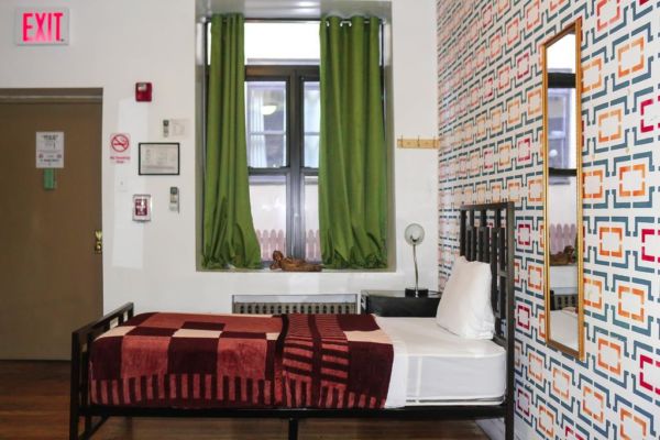 hostel room with patterned wall paper, twin bed and green curtains