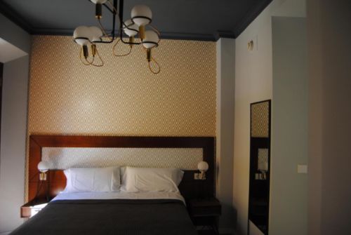 wood framed bed with blue blanket against yellow geometric patterned wall at Pension Cordoba, one of the best budget hotels in Seville