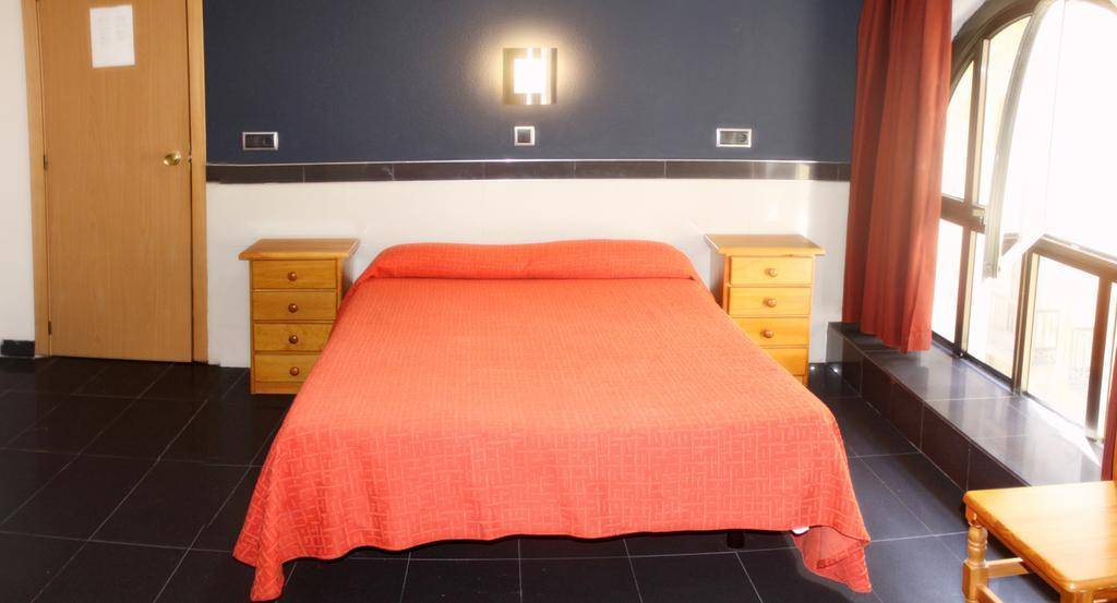 dark gray hotel room with red bedding and large semi-circle window