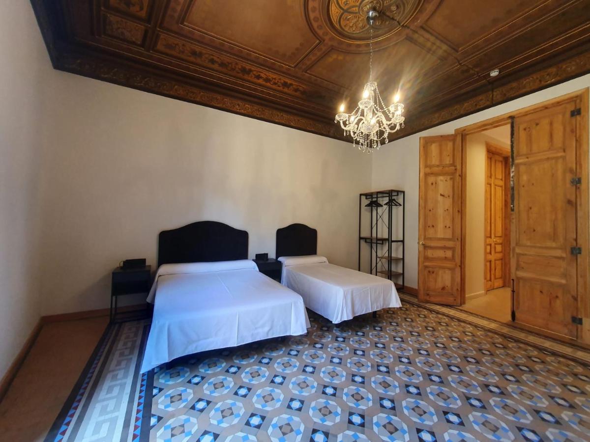 two beds in room with old patterned floor, carved wood ceiling and chandelier at Hostal Lausanne