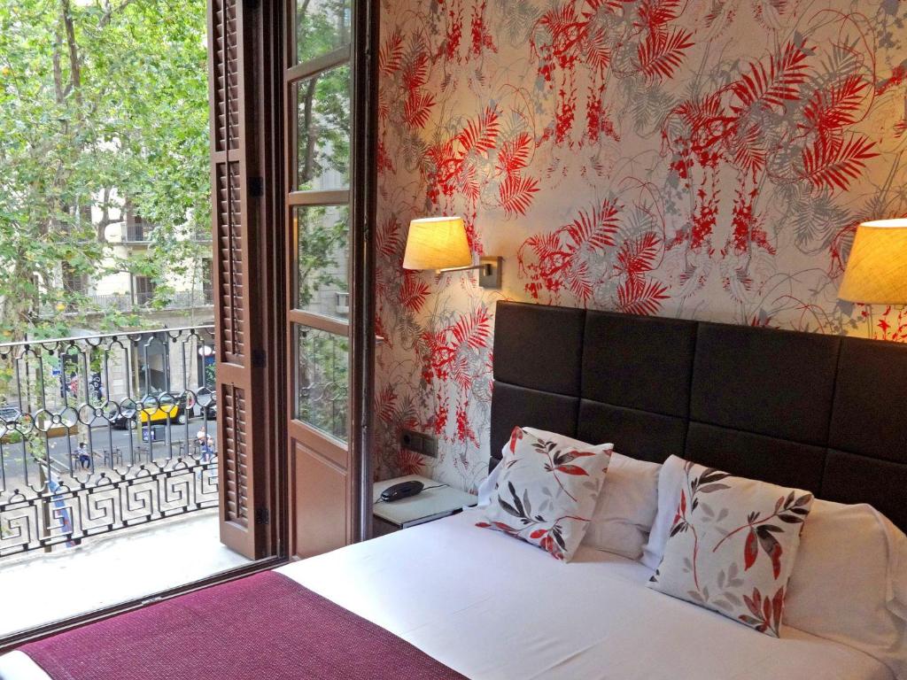 hotel room in Hotel Lloret Ramblas in Barcelona with floral wallpaper, large bed, and wood doors open to a private balcony