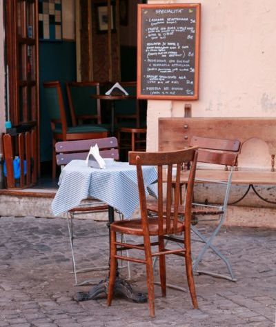 brown wood chairs and dining table outside restaurant with a chalkboard of daily special meals