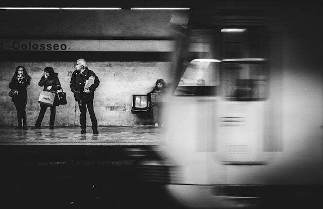 black and white photo of people waiting in metro station as a train approaches